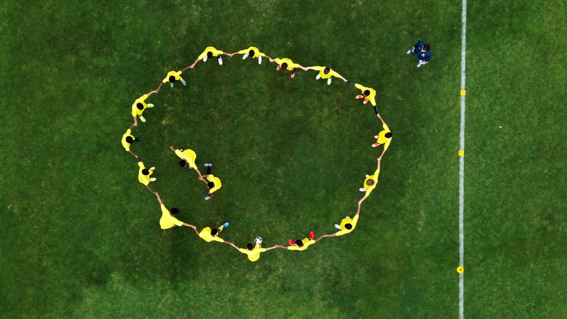 Top down aerial view of a youth soccer team forming a circle on a green field