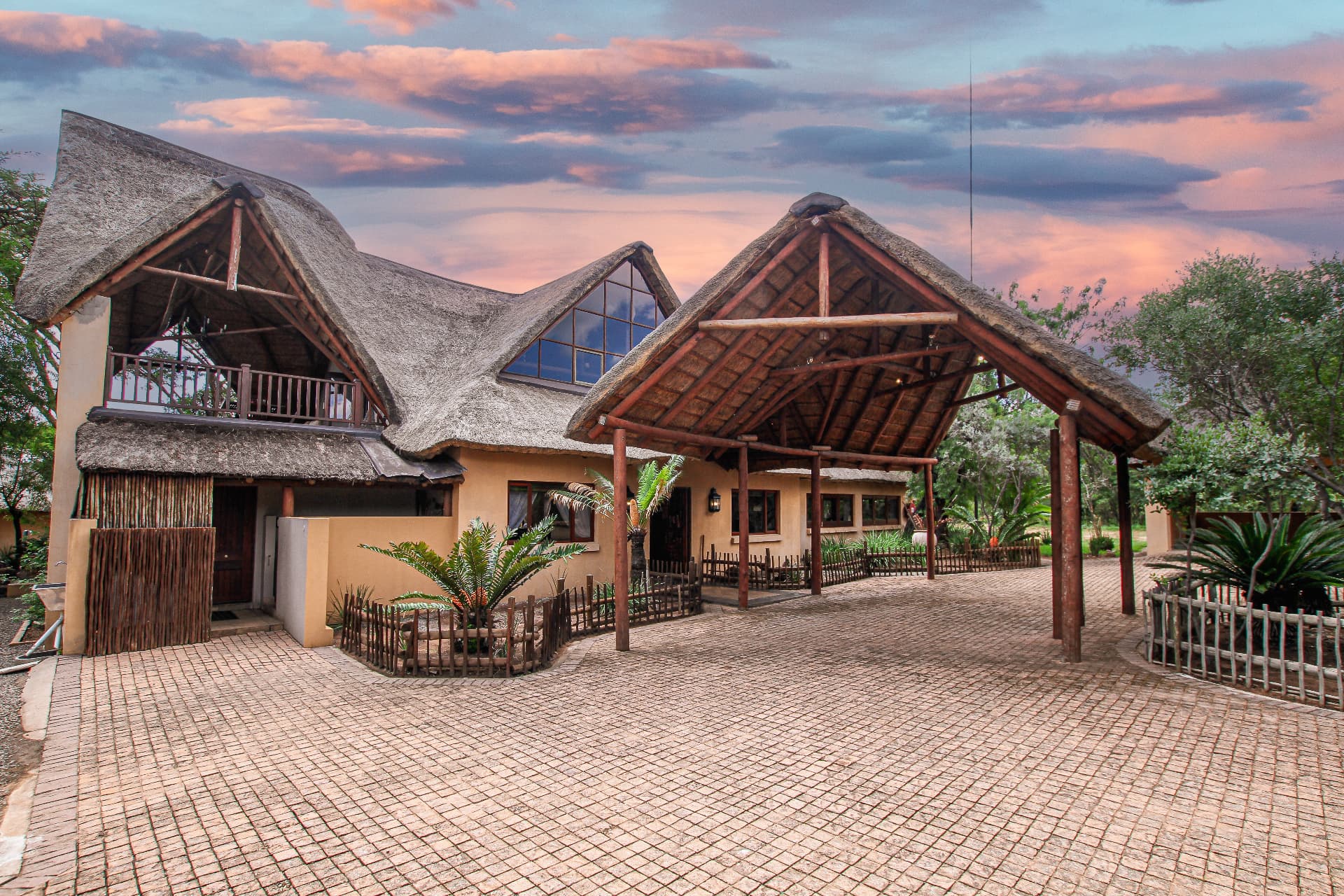 Traditional thatched safari lodge entrance with wooden pergola at sunset