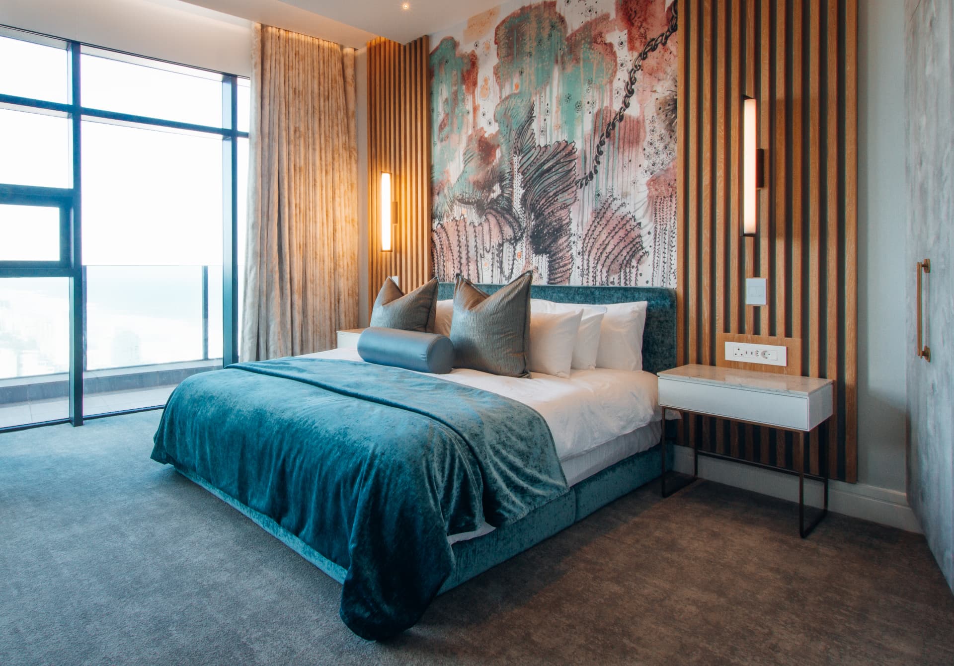 Ocean2 apartment bedroom with teal velvet bed, artwork feature wall and sea views